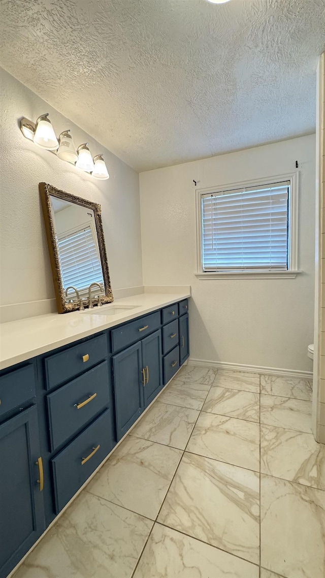 4801 Kent Ave, Groves, TX 77619 - bathroom featuring vanity, marble look tile flooring, baseboards, a textured ceiling, and toilet