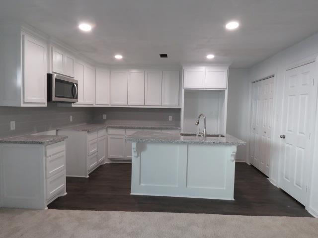 kitchen with light stone countertops, sink, white cabinetry, and an island with sink