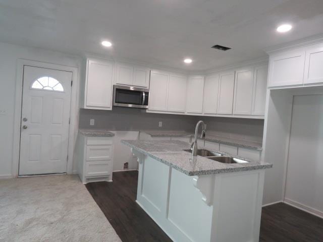 kitchen with sink, dark hardwood / wood-style floors, an island with sink, light stone counters, and white cabinetry