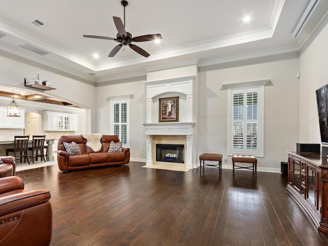 living room featuring a tray ceiling, a premium fireplace, dark wood-type flooring, and ceiling fan with notable chandelier