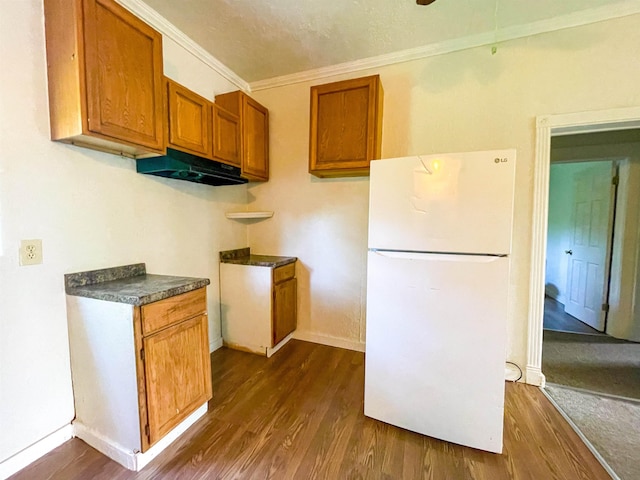 kitchen featuring freestanding refrigerator, under cabinet range hood, ornamental molding, dark wood-type flooring, and brown cabinets
