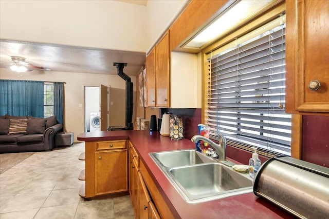 kitchen with a wood stove, sink, ceiling fan, light tile patterned flooring, and kitchen peninsula