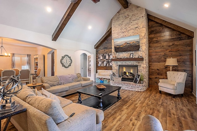 living room featuring beam ceiling, high vaulted ceiling, a chandelier, a fireplace, and hardwood / wood-style flooring