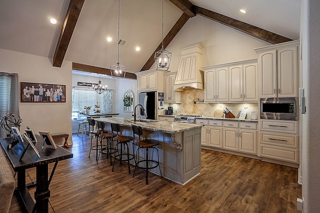 kitchen with backsplash, light stone counters, stainless steel appliances, decorative light fixtures, and an island with sink