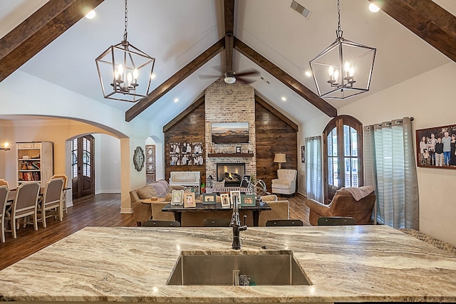 interior space featuring sink, beam ceiling, hardwood / wood-style flooring, high vaulted ceiling, and a stone fireplace