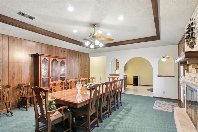 dining area featuring ceiling fan, a large fireplace, carpet floors, a textured ceiling, and wooden walls