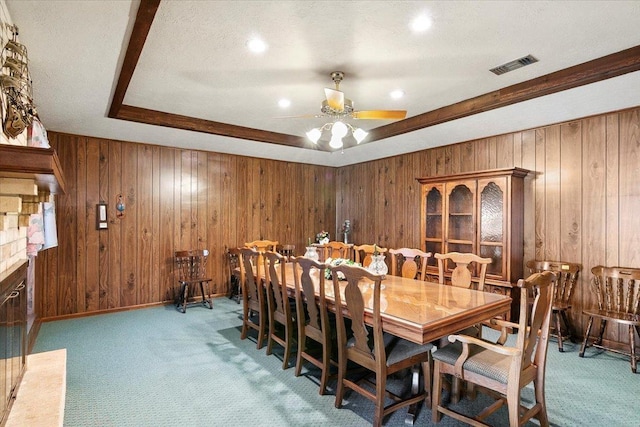 dining room featuring ceiling fan, wood walls, a textured ceiling, a tray ceiling, and carpet