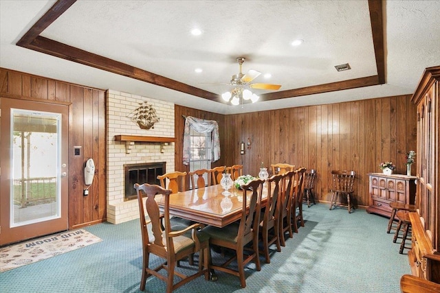 dining room featuring ceiling fan, a brick fireplace, wood walls, a textured ceiling, and dark carpet