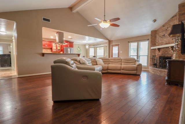 living room featuring beamed ceiling, dark hardwood / wood-style flooring, a brick fireplace, and ceiling fan