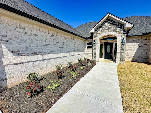 doorway to property with brick siding, stone siding, and a shingled roof