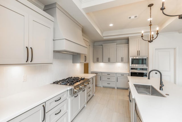 kitchen with crown molding, a sink, a tray ceiling, appliances with stainless steel finishes, and visible vents