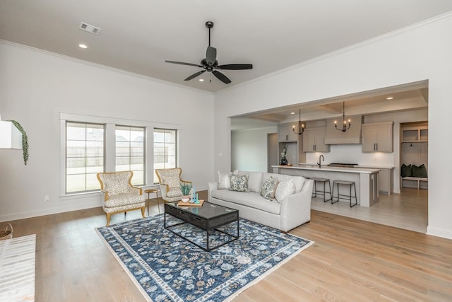 living area with light wood-type flooring, ceiling fan with notable chandelier, visible vents, and crown molding