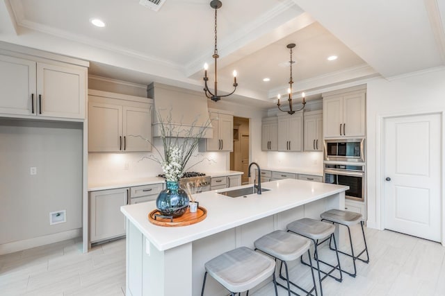 kitchen with stainless steel appliances, a raised ceiling, gray cabinets, a sink, and crown molding