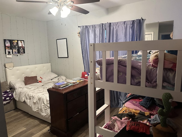 bedroom featuring hardwood / wood-style floors, ceiling fan, and wood walls