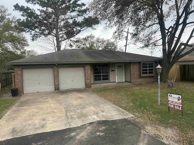 ranch-style home with brick siding, an attached garage, driveway, and fence