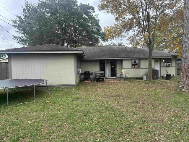 rear view of property featuring a lawn and a trampoline