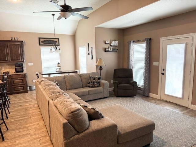 living room featuring vaulted ceiling, ceiling fan with notable chandelier, and light wood-type flooring