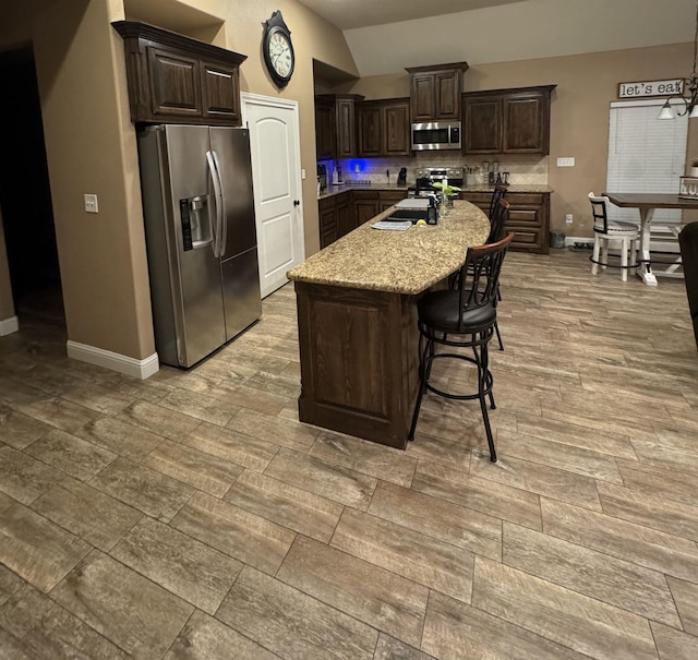 kitchen featuring dark brown cabinets, stainless steel appliances, lofted ceiling, and an island with sink