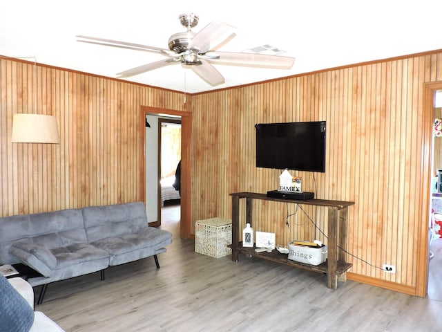 living area with visible vents, ceiling fan, wood walls, and wood finished floors