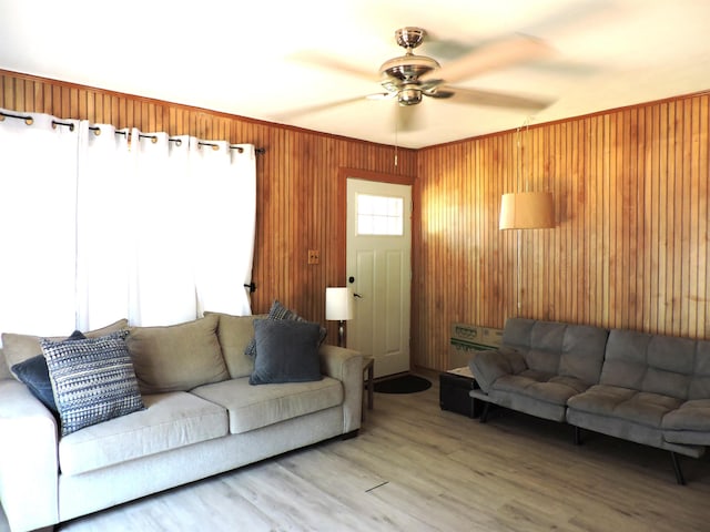 living room featuring a ceiling fan, wood walls, and light wood-style flooring