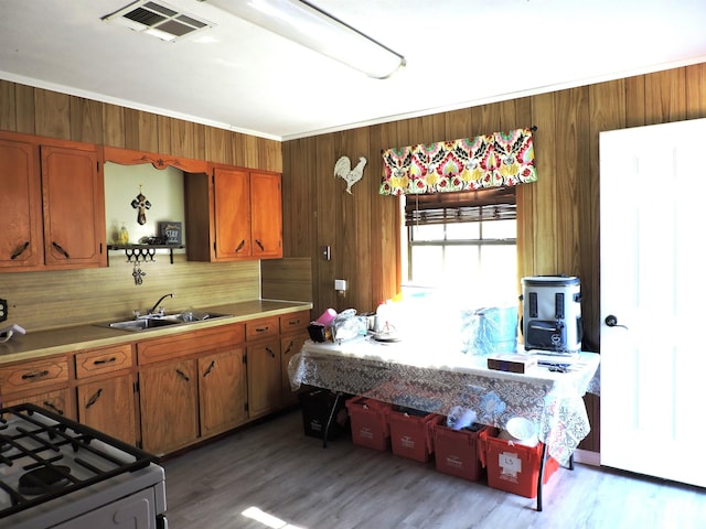 kitchen with wood walls, a sink, visible vents, light countertops, and brown cabinets