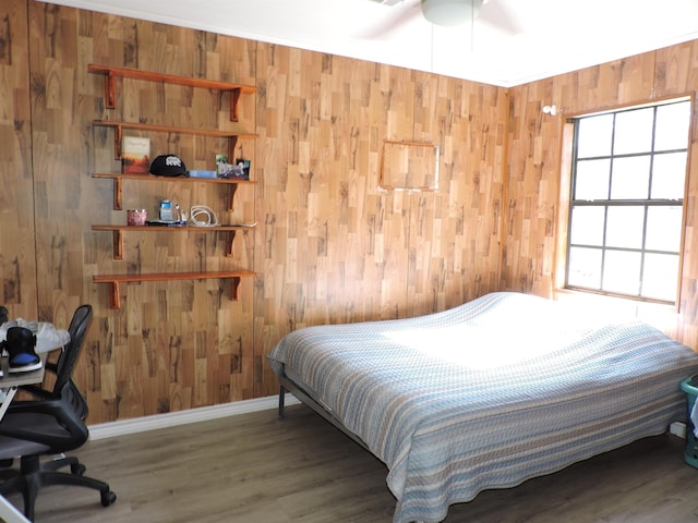 bedroom featuring a ceiling fan, wooden walls, baseboards, and wood finished floors