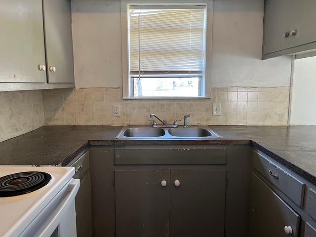 kitchen with dark countertops, white range with electric cooktop, backsplash, and a sink