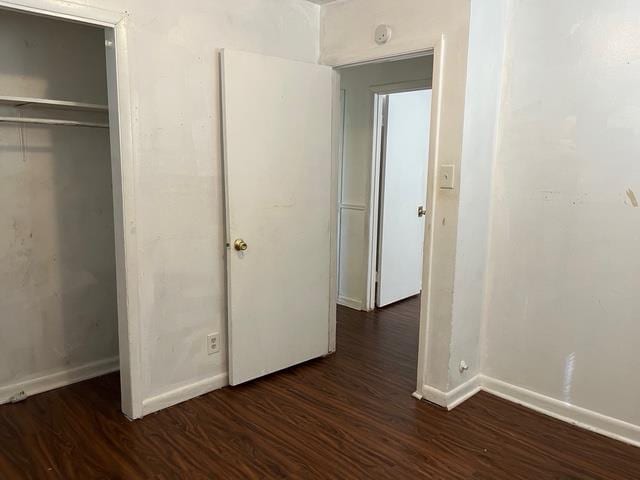 unfurnished bedroom with dark wood-style floors, baseboards, and a closet