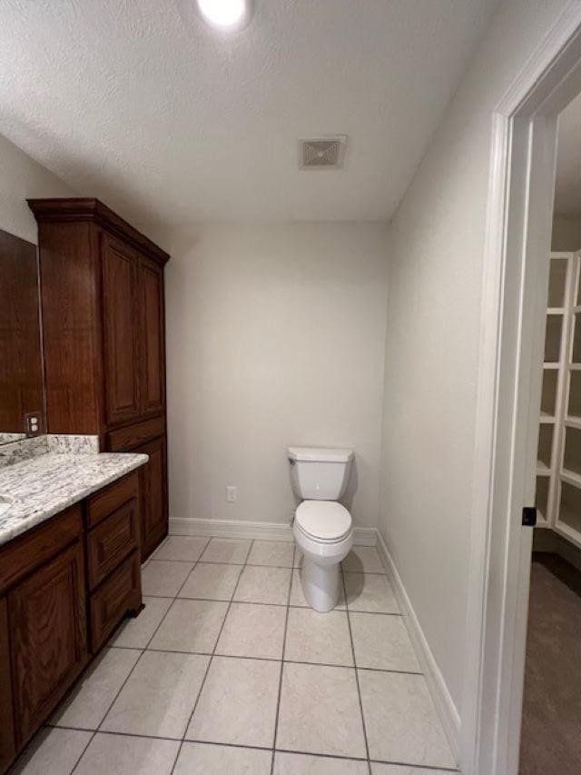 bathroom featuring baseboards, visible vents, toilet, tile patterned floors, and a walk in closet