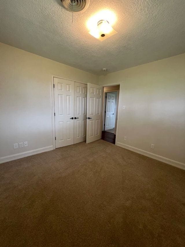 unfurnished bedroom featuring a textured ceiling, visible vents, baseboards, a closet, and dark colored carpet