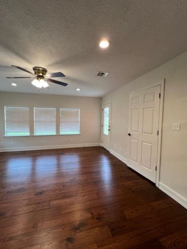 empty room with dark wood-style floors, visible vents, baseboards, and a ceiling fan