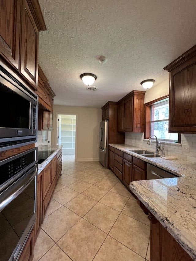 kitchen featuring stainless steel appliances, light stone counters, a sink, and tasteful backsplash