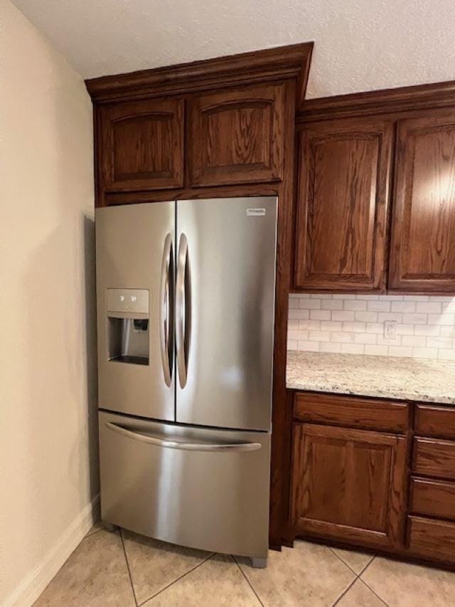 kitchen featuring light tile patterned floors, light stone counters, baseboards, backsplash, and stainless steel fridge