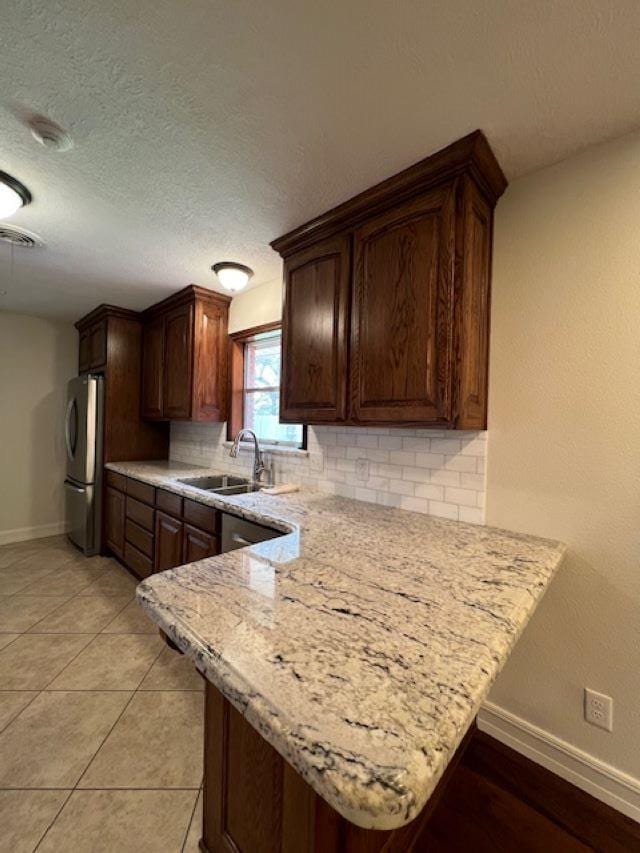 kitchen featuring light stone counters, backsplash, freestanding refrigerator, a sink, and a peninsula