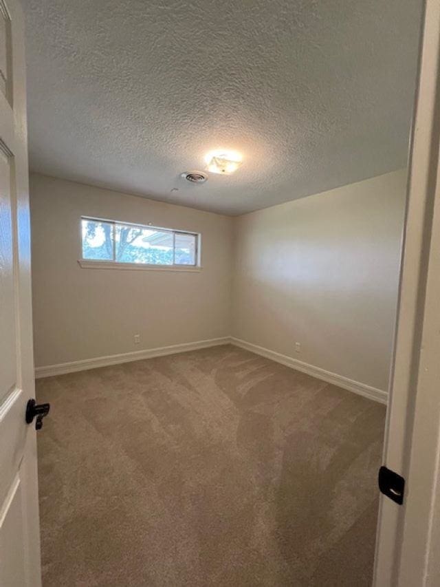 empty room with carpet, baseboards, and a textured ceiling