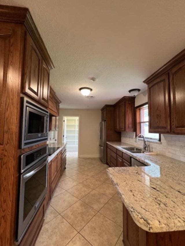 kitchen with stainless steel appliances, tasteful backsplash, light tile patterned flooring, a sink, and light stone countertops