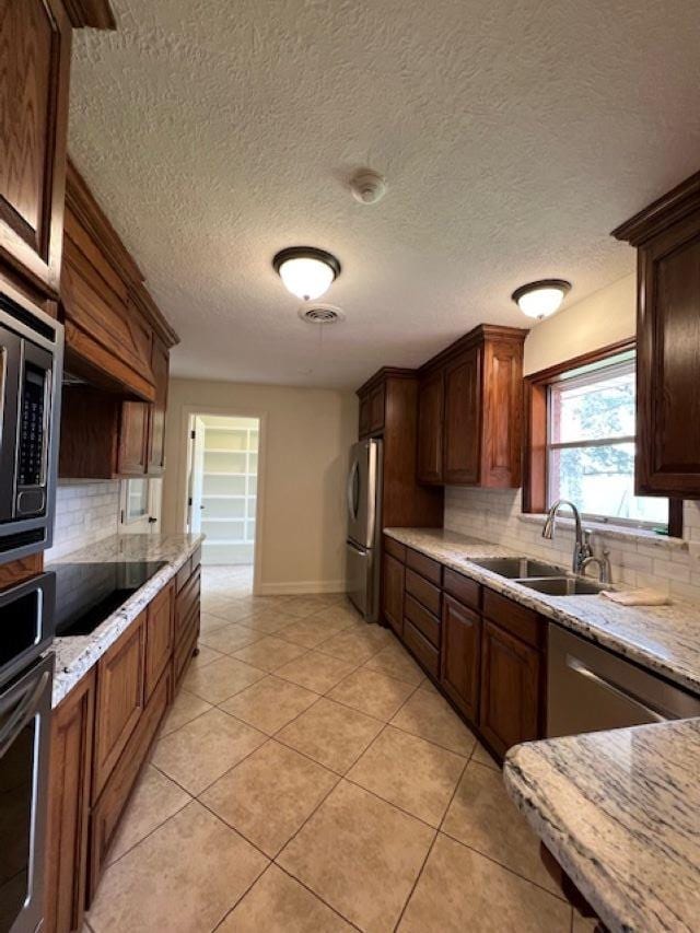 kitchen featuring appliances with stainless steel finishes, tasteful backsplash, a sink, and light tile patterned floors