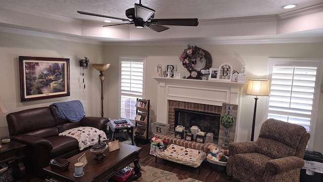 living area featuring a tray ceiling, a textured ceiling, wood finished floors, crown molding, and a brick fireplace