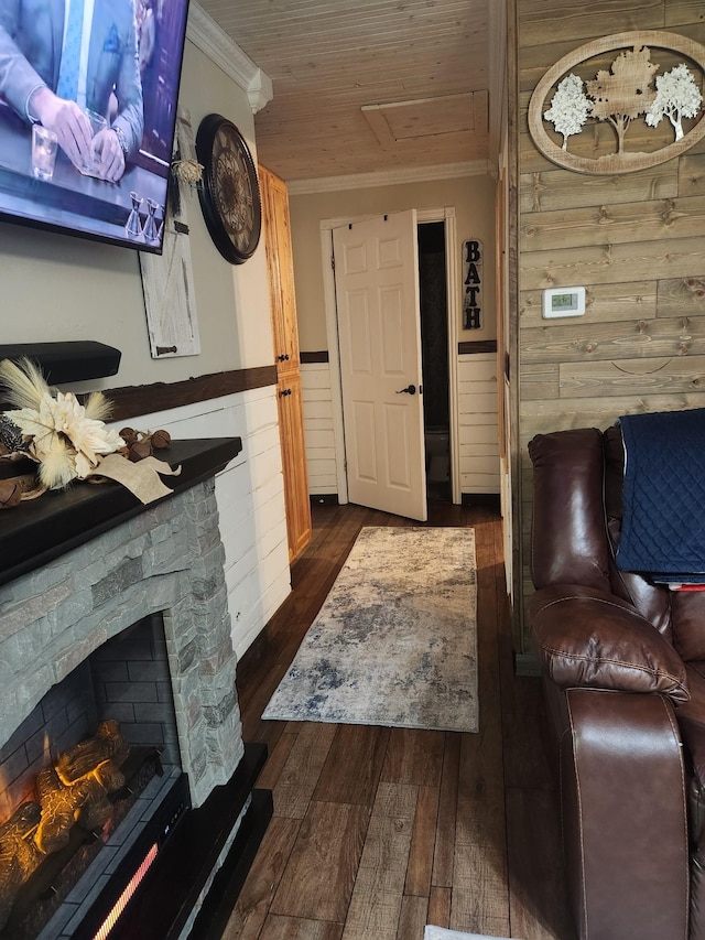 living room featuring dark wood-type flooring, wooden ceiling, a stone fireplace, crown molding, and wooden walls