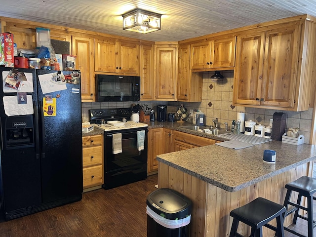 kitchen featuring kitchen peninsula, dark hardwood / wood-style flooring, sink, black appliances, and a breakfast bar area