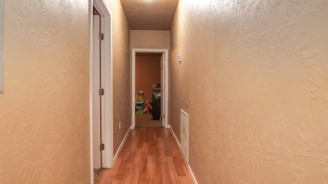 corridor with visible vents, light wood-style flooring, and a textured wall