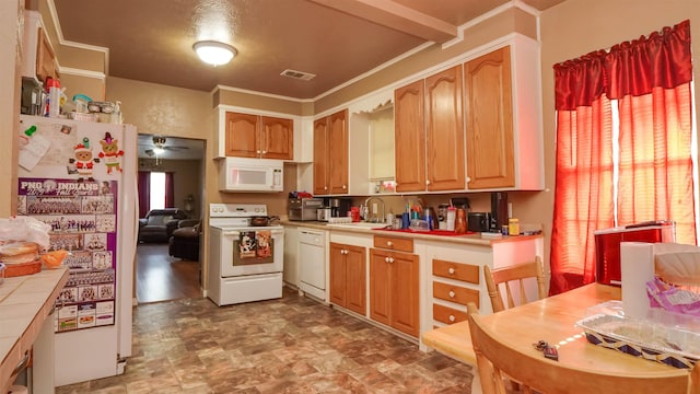 kitchen featuring a sink, tile counters, visible vents, stone finish floor, and white appliances