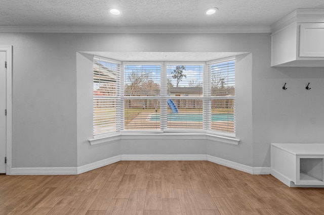 unfurnished dining area featuring crown molding, light hardwood / wood-style floors, and a textured ceiling