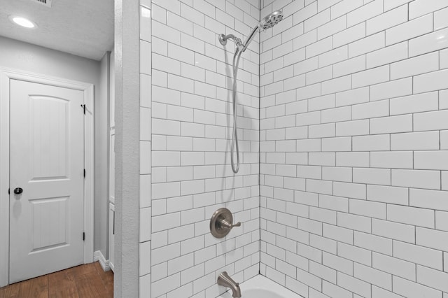 bathroom featuring hardwood / wood-style flooring, a textured ceiling, and tiled shower / bath