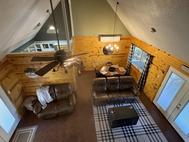 interior space with a textured ceiling, ceiling fan, vaulted ceiling, and wood walls