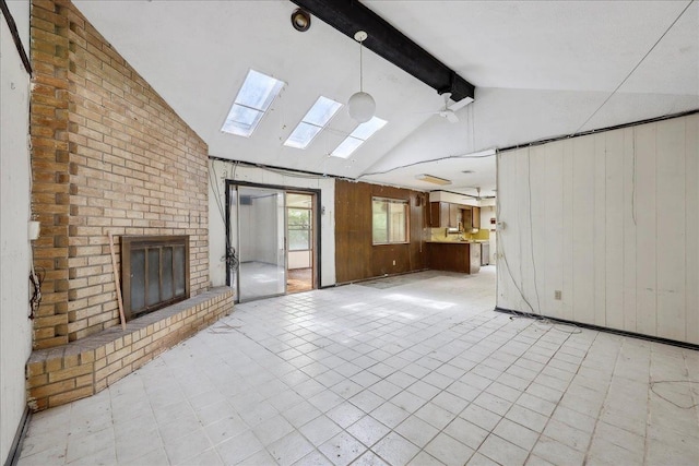 unfurnished living room featuring wood walls, vaulted ceiling with skylight, and a fireplace
