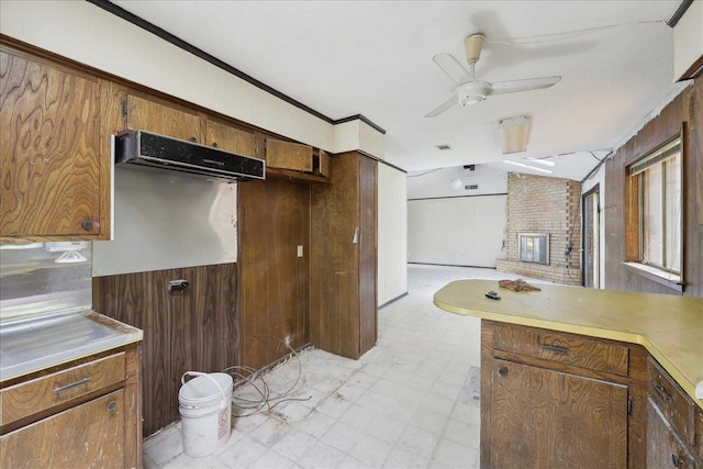 kitchen with a fireplace, ceiling fan, light countertops, wooden walls, and light floors