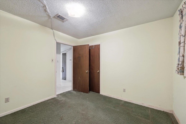 carpeted empty room featuring a textured ceiling, visible vents, and baseboards