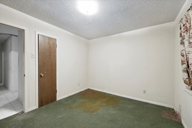 carpeted spare room featuring a textured ceiling and baseboards