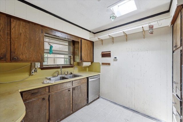 kitchen featuring a sink, wood walls, light countertops, stainless steel dishwasher, and light floors